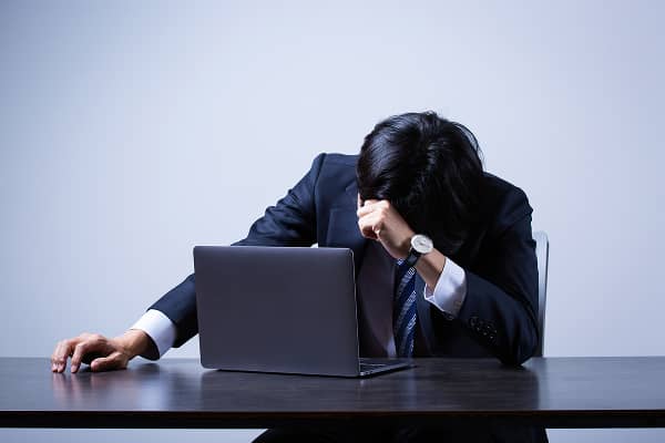 ノートパソコンの前で頭を抱えて落ち込むスーツ姿の男性