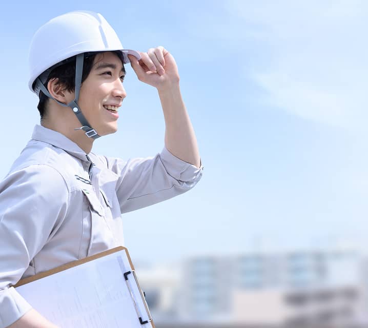 建設現場でヘルメットをかぶり、空を見上げて笑顔を見せる男性