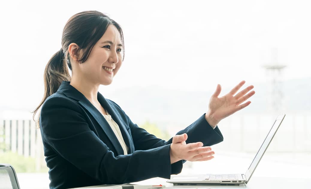 ビジネススーツを着た女性がノートパソコンの前で笑顔でプレゼンしているシーン