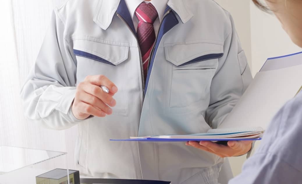 業服を着た男性が資料を手に取り、相手に指示や説明をしている場面