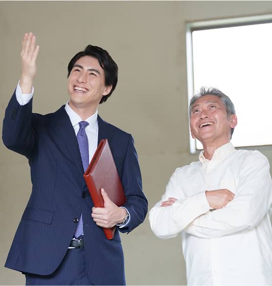 スーツ姿の男性が室内で高齢の男性に説明をしながら笑顔で話す様子