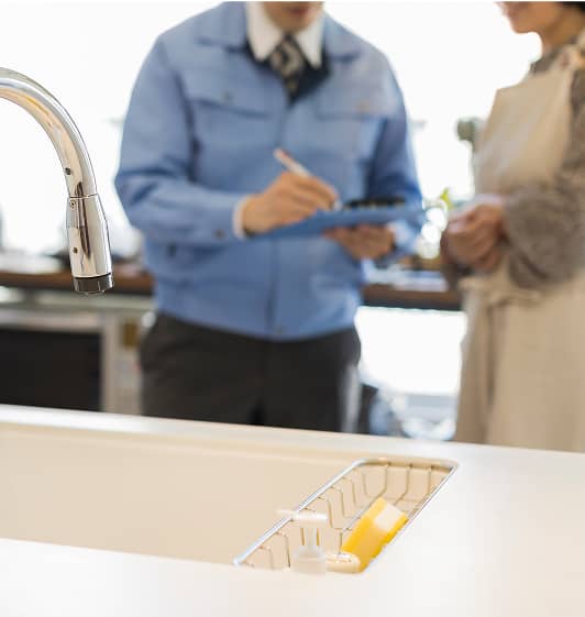 キッチンで点検中の作業員とそれを見守る住人