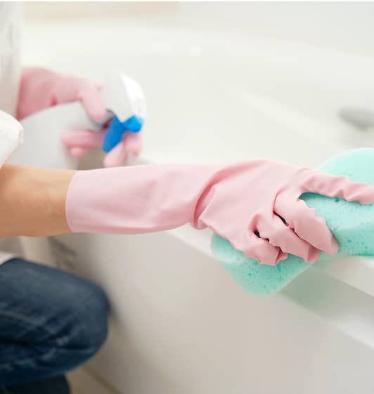 ピンクのゴム手袋をした手で浴槽を掃除している様子