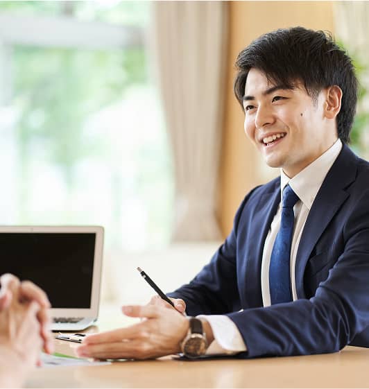スーツ姿の若い男性が笑顔で相談に応じている場面