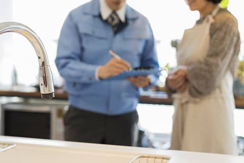 キッチンで修理内容について説明する作業員と話す女性