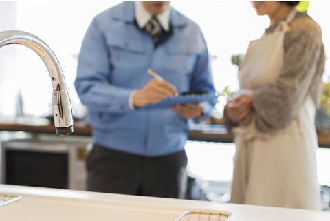 キッチンで点検報告を行う作業員とそれを聞く住人の様子