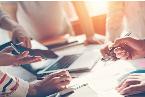 複数人が資料やPCを囲んで会議をしている様子