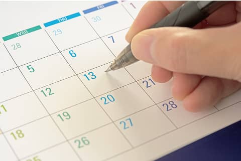 カレンダーの13日にペンで予定を書き込んでいる手元