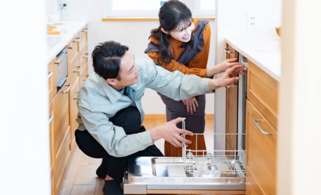 作業服姿のスタッフが女性に食洗機の使い方を説明している場面